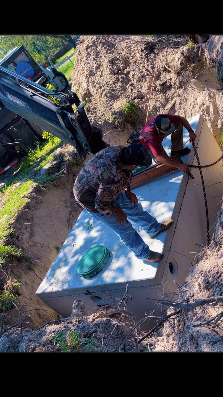 Technicians guiding a septic tank into the excavation